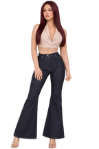 Woman wearing a beige top and black flared jeans on a white background