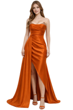 Woman wearing a strapless orange evening gown with a slit on a white background